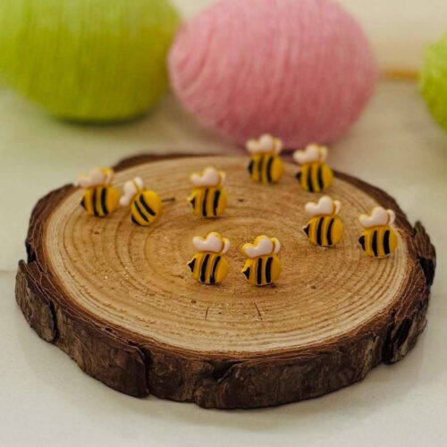 Bee Stud Earrings displayed on a rustic wood slice, featuring tiny yellow and black bumblebees with white wings, perfect for springtime wear.